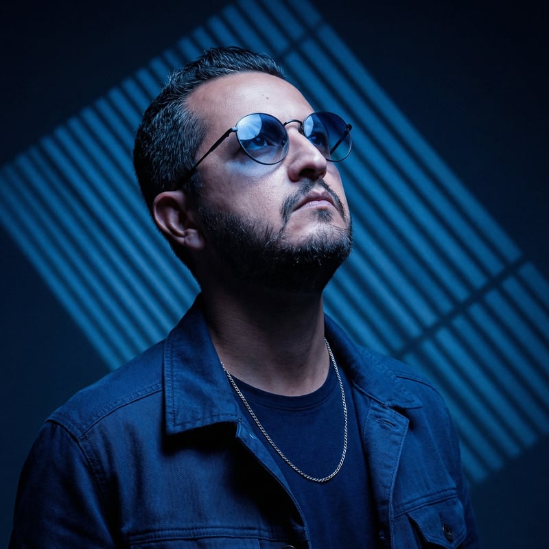 André Alves, retrato com luz azul e óculos de lentes azuis, olhando para cima